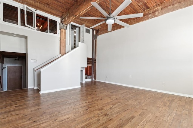 unfurnished living room featuring a towering ceiling, beamed ceiling, hardwood / wood-style flooring, ceiling fan, and wooden ceiling