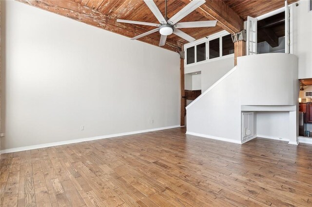 unfurnished living room with wood ceiling, beamed ceiling, ceiling fan, hardwood / wood-style floors, and a high ceiling