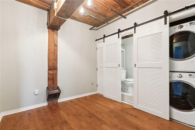 clothes washing area featuring stacked washer / dryer, a barn door, hardwood / wood-style floors, and wooden ceiling