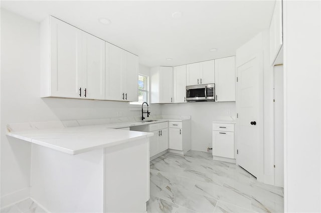 kitchen with marble finish floor, a sink, stainless steel microwave, a peninsula, and white cabinets