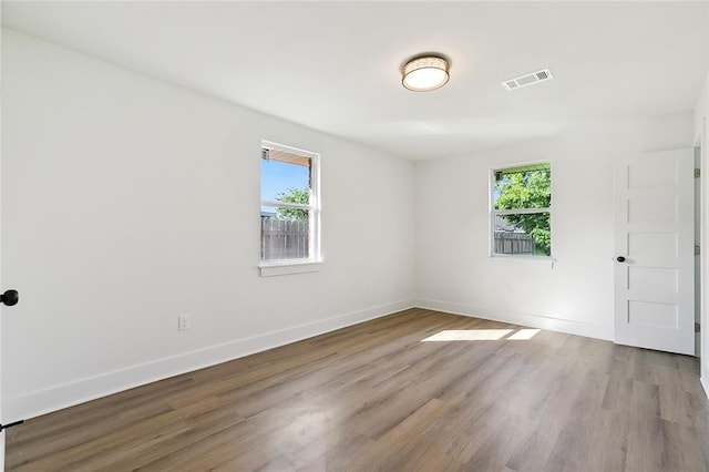 empty room featuring plenty of natural light, wood finished floors, visible vents, and baseboards