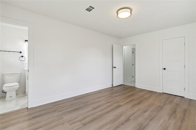 unfurnished bedroom featuring light wood-style flooring, baseboards, visible vents, and ensuite bathroom