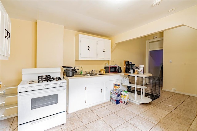 kitchen with white range with gas cooktop, light tile patterned floors, sink, and white cabinets