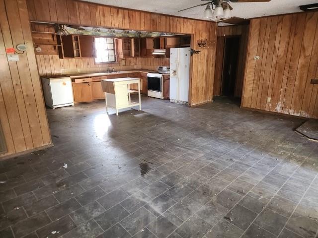 kitchen with sink, white appliances, ceiling fan, a kitchen island, and wood walls