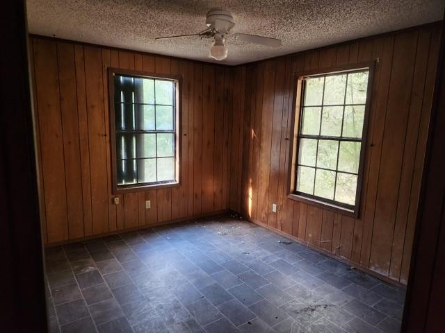 spare room with ceiling fan, wooden walls, and a textured ceiling