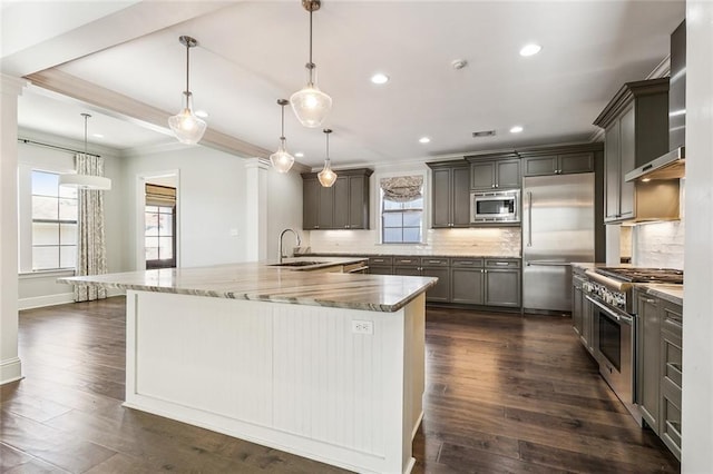 kitchen featuring hanging light fixtures, built in appliances, backsplash, and a large island with sink