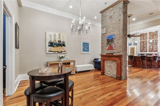 dining room featuring a stone fireplace, crown molding, indoor bar, ceiling fan, and light hardwood / wood-style floors