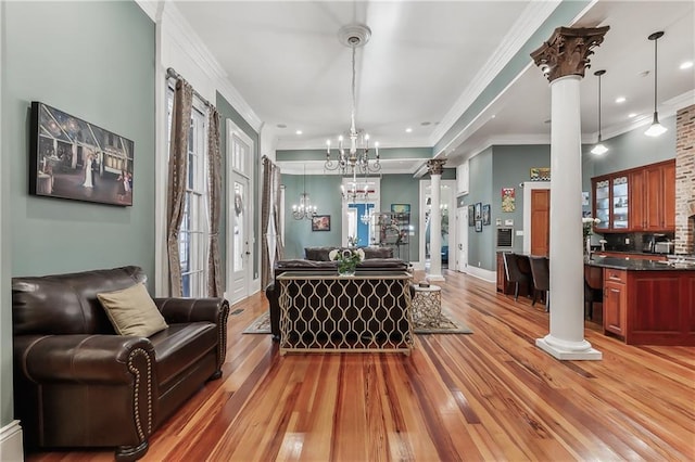 interior space with ornate columns, crown molding, a chandelier, and light hardwood / wood-style floors