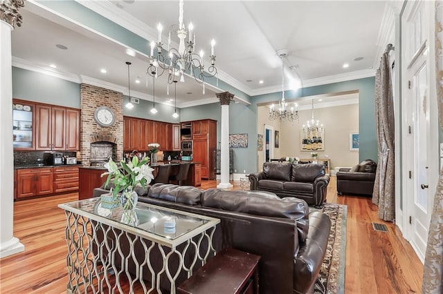 living room featuring an inviting chandelier, crown molding, decorative columns, and light wood-type flooring