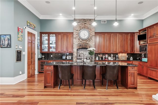 kitchen with stainless steel microwave, a kitchen bar, decorative light fixtures, and an island with sink