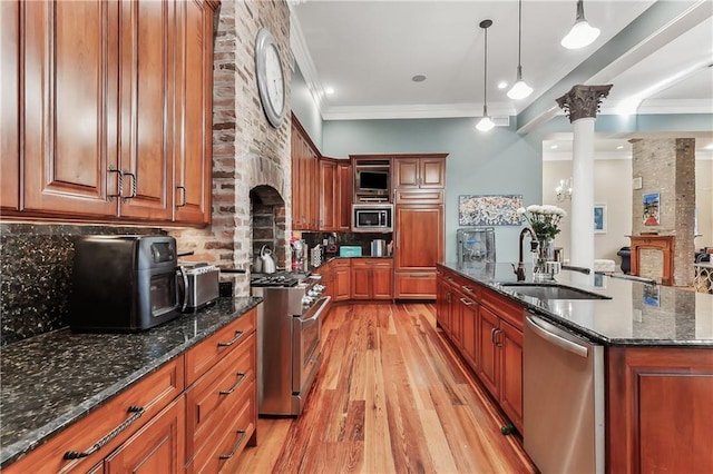 kitchen featuring decorative light fixtures, sink, dark stone countertops, stainless steel appliances, and crown molding