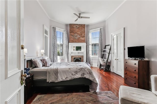 bedroom featuring crown molding, ceiling fan, hardwood / wood-style floors, and a brick fireplace