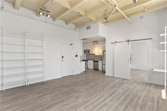 835 Julia St Unit 18, New Orleans, LA 70113 - unfurnished living room with a barn door, light wood-style floors, beamed ceiling, a high ceiling, and baseboards