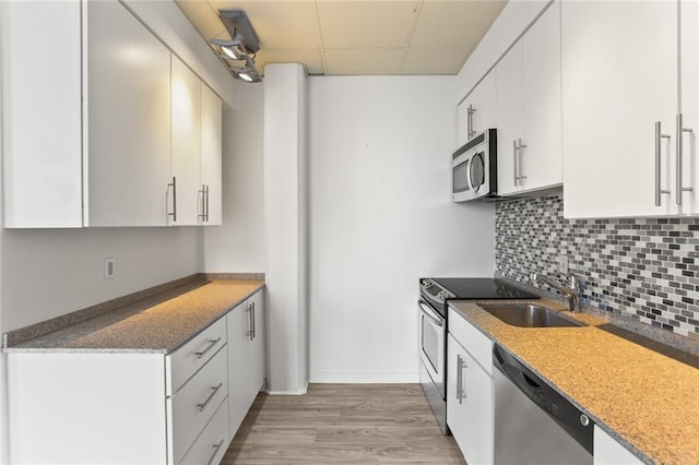 835 Julia St Unit 18, New Orleans, LA 70113 - kitchen featuring appliances with stainless steel finishes, a sink, light wood-style flooring, decorative backsplash, and a paneled ceiling