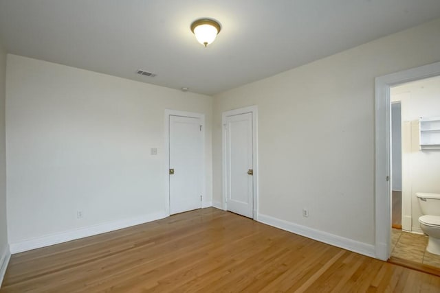 unfurnished bedroom featuring ensuite bathroom and wood-type flooring