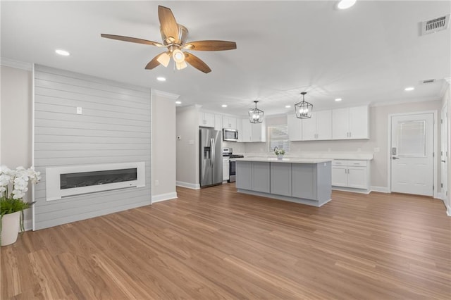 kitchen with appliances with stainless steel finishes, a fireplace, white cabinets, a kitchen island, and decorative light fixtures