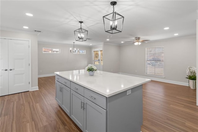 kitchen featuring gray cabinets, wood-type flooring, ornamental molding, a kitchen island, and decorative light fixtures