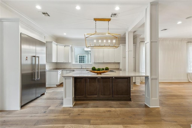 kitchen with white cabinetry, hanging light fixtures, a kitchen island, and stainless steel built in refrigerator