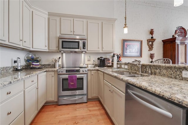 kitchen featuring appliances with stainless steel finishes, decorative light fixtures, sink, light hardwood / wood-style floors, and light stone countertops