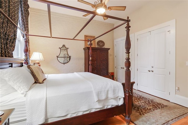 bedroom featuring hardwood / wood-style flooring, a closet, ceiling fan, and brick wall