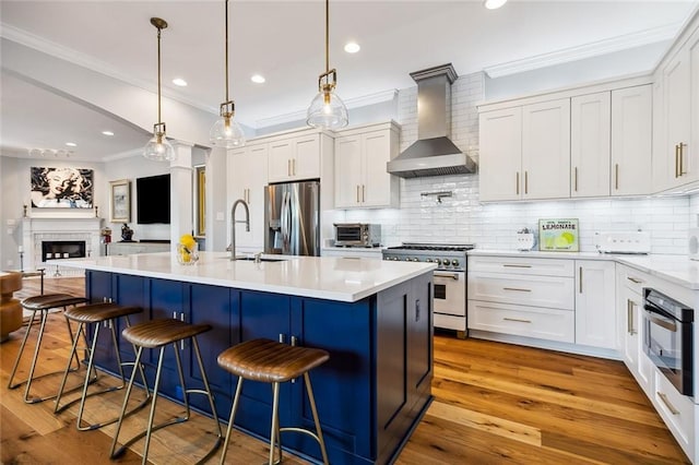 kitchen with white cabinetry, wall chimney range hood, an island with sink, and appliances with stainless steel finishes