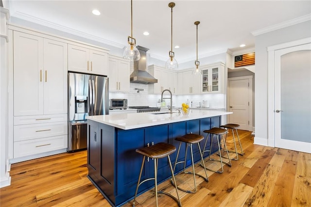 kitchen with decorative light fixtures, white cabinetry, stainless steel fridge with ice dispenser, wall chimney range hood, and light hardwood / wood-style flooring