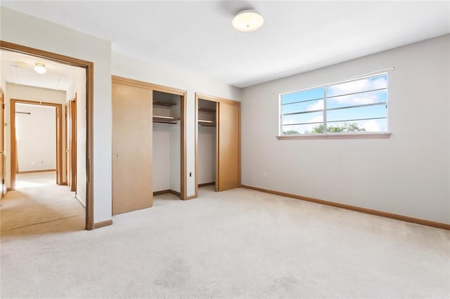 unfurnished bedroom featuring multiple closets and light colored carpet