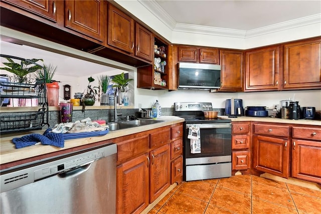 kitchen with light tile patterned flooring, ornamental molding, appliances with stainless steel finishes, and sink