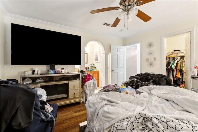 bedroom with ornamental molding, a spacious closet, ceiling fan, dark wood-type flooring, and a closet