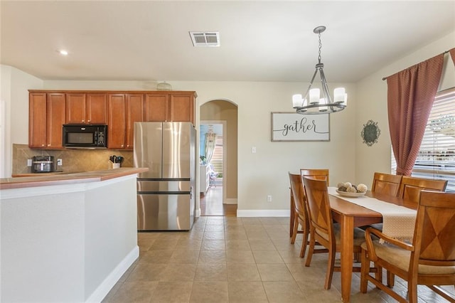 kitchen with light tile patterned flooring, an inviting chandelier, tasteful backsplash, decorative light fixtures, and stainless steel refrigerator