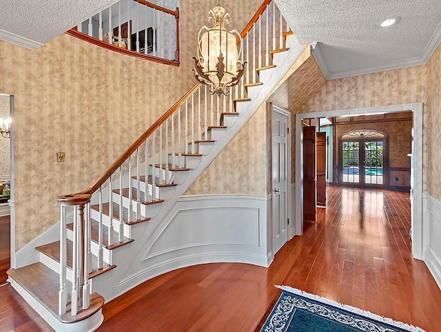 stairway featuring french doors, wood-type flooring, a textured ceiling, ornamental molding, and a notable chandelier