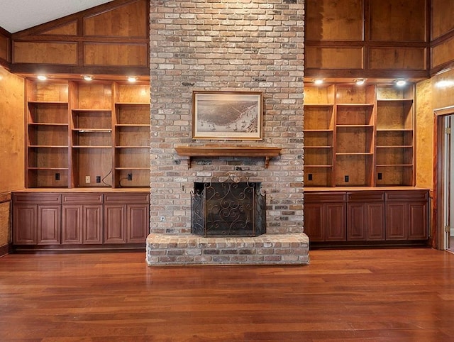 unfurnished living room with vaulted ceiling, built in features, wooden walls, a fireplace, and wood-type flooring