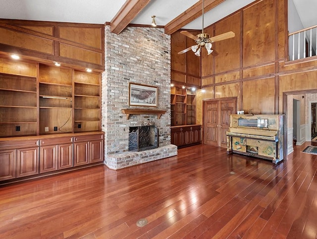 unfurnished living room with beam ceiling, wooden walls, dark hardwood / wood-style floors, a fireplace, and built in shelves