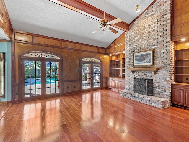 unfurnished living room featuring french doors, vaulted ceiling, light hardwood / wood-style flooring, a brick fireplace, and a textured ceiling