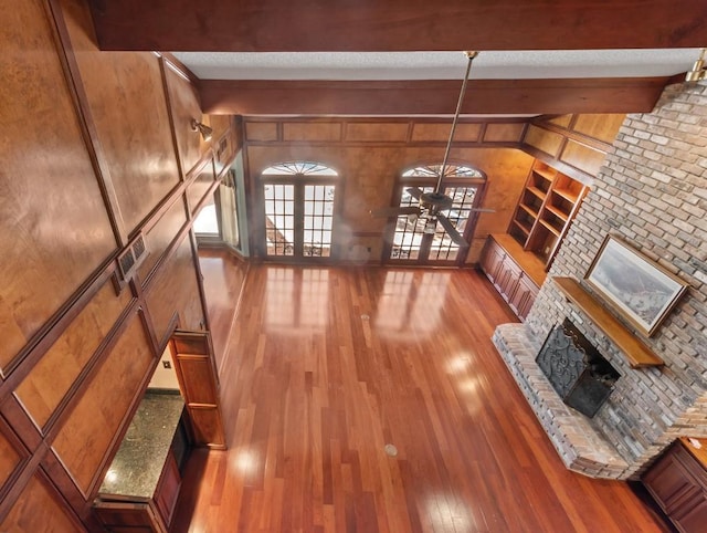 unfurnished living room with a brick fireplace, wooden walls, light hardwood / wood-style floors, and beam ceiling