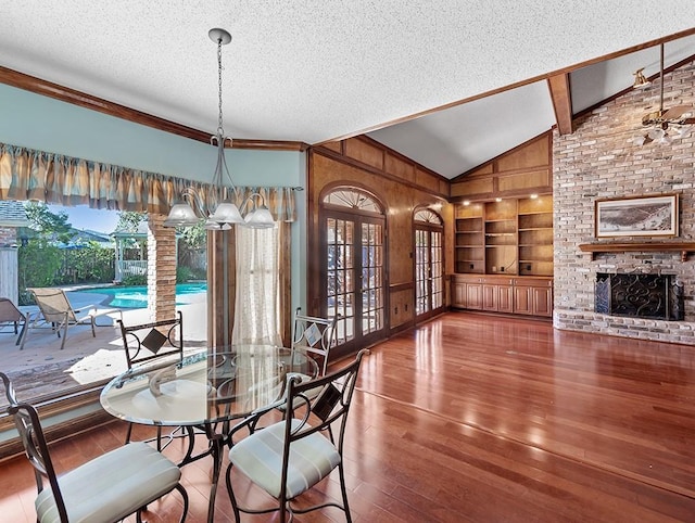 dining space with vaulted ceiling, wood-type flooring, a brick fireplace, a textured ceiling, and built in shelves