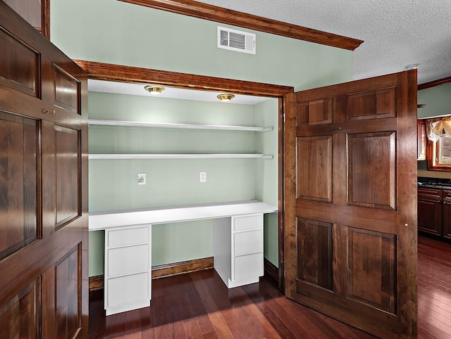 unfurnished office with dark hardwood / wood-style flooring, built in desk, and a textured ceiling