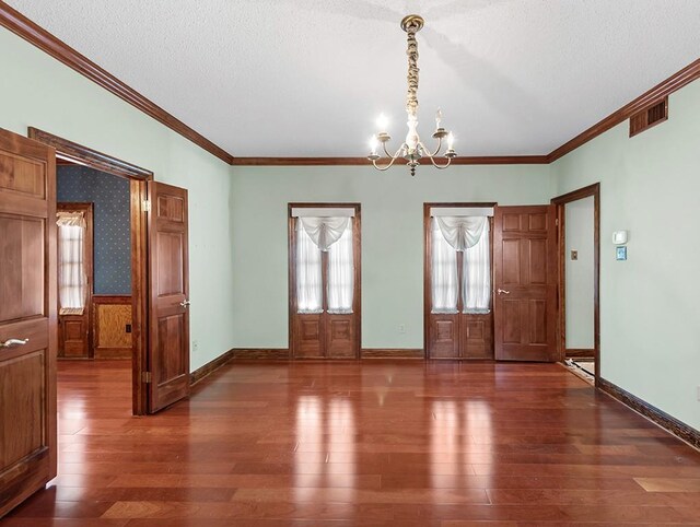 empty room featuring dark hardwood / wood-style flooring, a notable chandelier, crown molding, and a textured ceiling