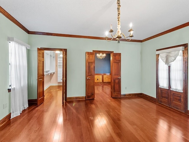 empty room featuring ornamental molding, hardwood / wood-style floors, a textured ceiling, and a notable chandelier