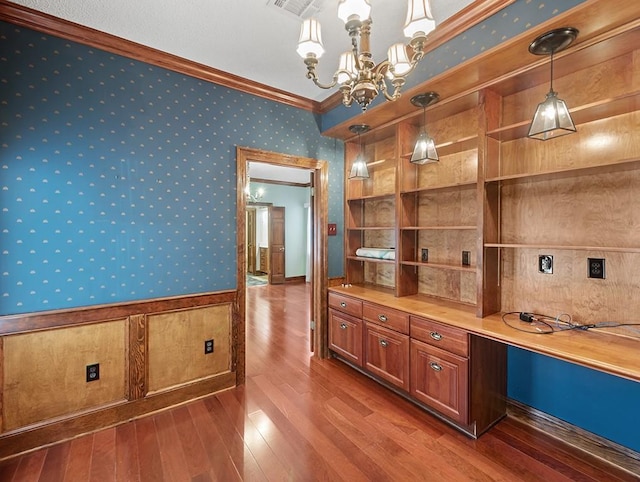 bar featuring crown molding, dark wood-type flooring, an inviting chandelier, built in desk, and decorative light fixtures