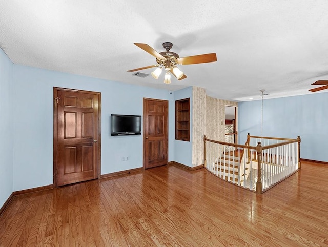 empty room with ceiling fan, wood-type flooring, and a textured ceiling