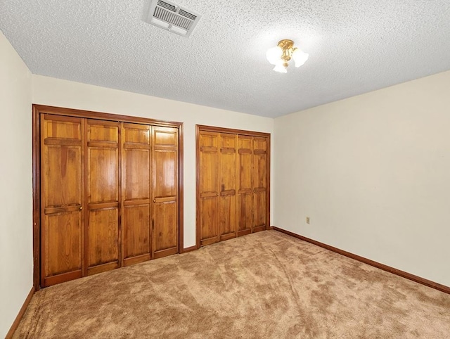 unfurnished bedroom with light carpet, two closets, and a textured ceiling