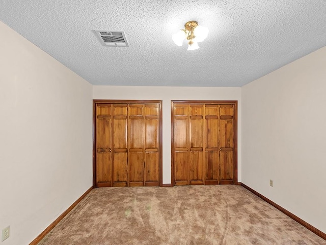 unfurnished bedroom with light colored carpet, a textured ceiling, and two closets