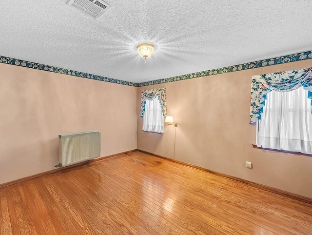 spare room featuring radiator, hardwood / wood-style flooring, a textured ceiling, and a healthy amount of sunlight