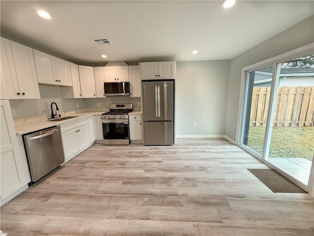 kitchen featuring white cabinetry, sink, stainless steel appliances, a healthy amount of sunlight, and light hardwood / wood-style flooring