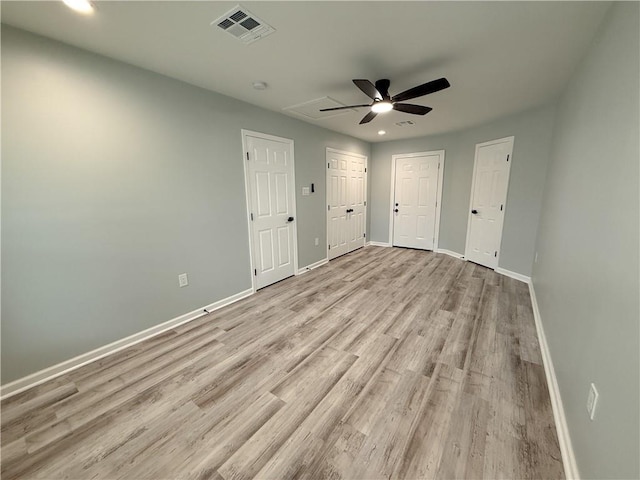 unfurnished bedroom with light wood-type flooring, two closets, and ceiling fan