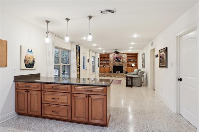 kitchen featuring dark stone countertops, hanging light fixtures, built in features, and a brick fireplace