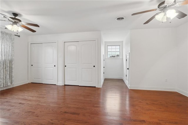 unfurnished bedroom with dark hardwood / wood-style floors, two closets, and ceiling fan