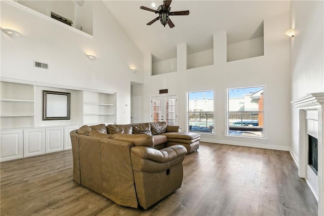 living room featuring a towering ceiling, built in features, hardwood / wood-style flooring, ceiling fan, and french doors