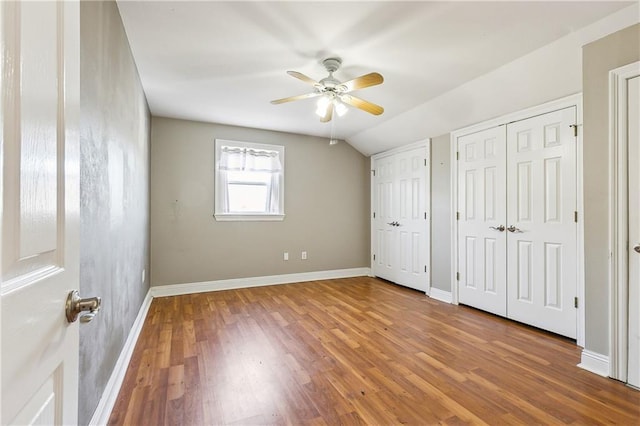 unfurnished bedroom featuring ceiling fan, wood-type flooring, vaulted ceiling, and two closets